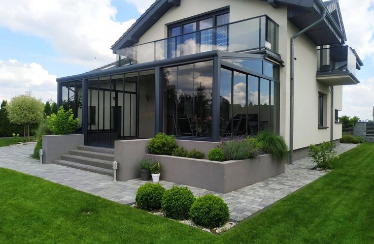 Moderní zimní zahrada z hliníkové konstrukce v antracitové barvě rozšiřuje obytný prostor domu a nabízí celoroční využití s maximálním prosvětlením a výhledem do zahrady.
