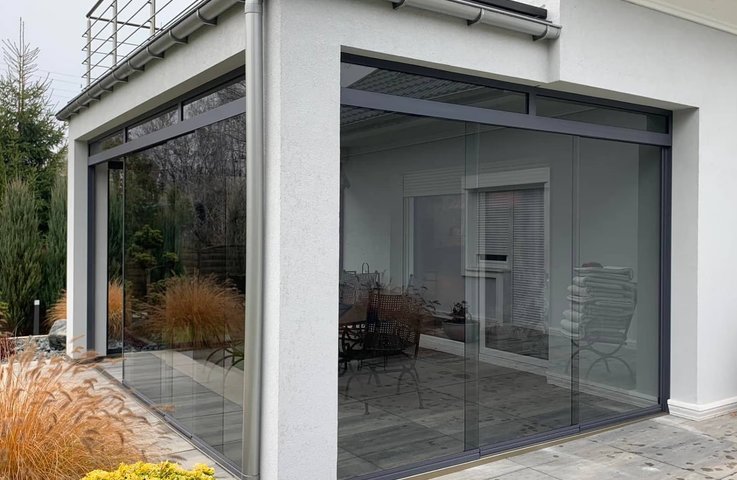 Elegantní bezrámové zasklení zimní zahrady v moderním designu. Prosklené stěny s maximální průhledností zajišťují dokonalé propojení interiéru s exteriérem. Ideální řešení pro zimní zahrady, pergoly a terasy od Hezký stín – kombinace estetiky, funkčnosti a nadčasového vzhledu.