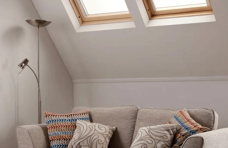 Podkrovní obývací pokoj s dvojicí střešních oken vybavených zatemňovacími roletami. Rolety zlepšují stínění, brání přehřívání místnosti a vytvářejí příjemné prostředí pro odpočinek i večerní hraní na kytaru.