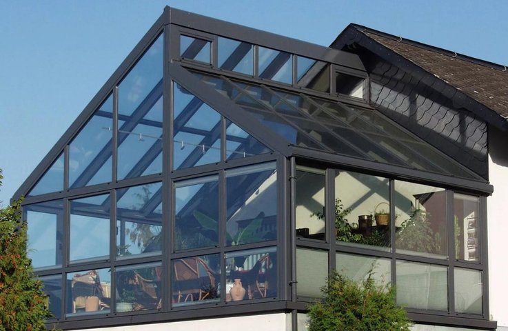 Velkorysá celoroční zimní zahrada z hliníku a skla v patře rodinného domu, s vysokým šikmým prosklením a výhledem do okolí – realizace Hezký stín.